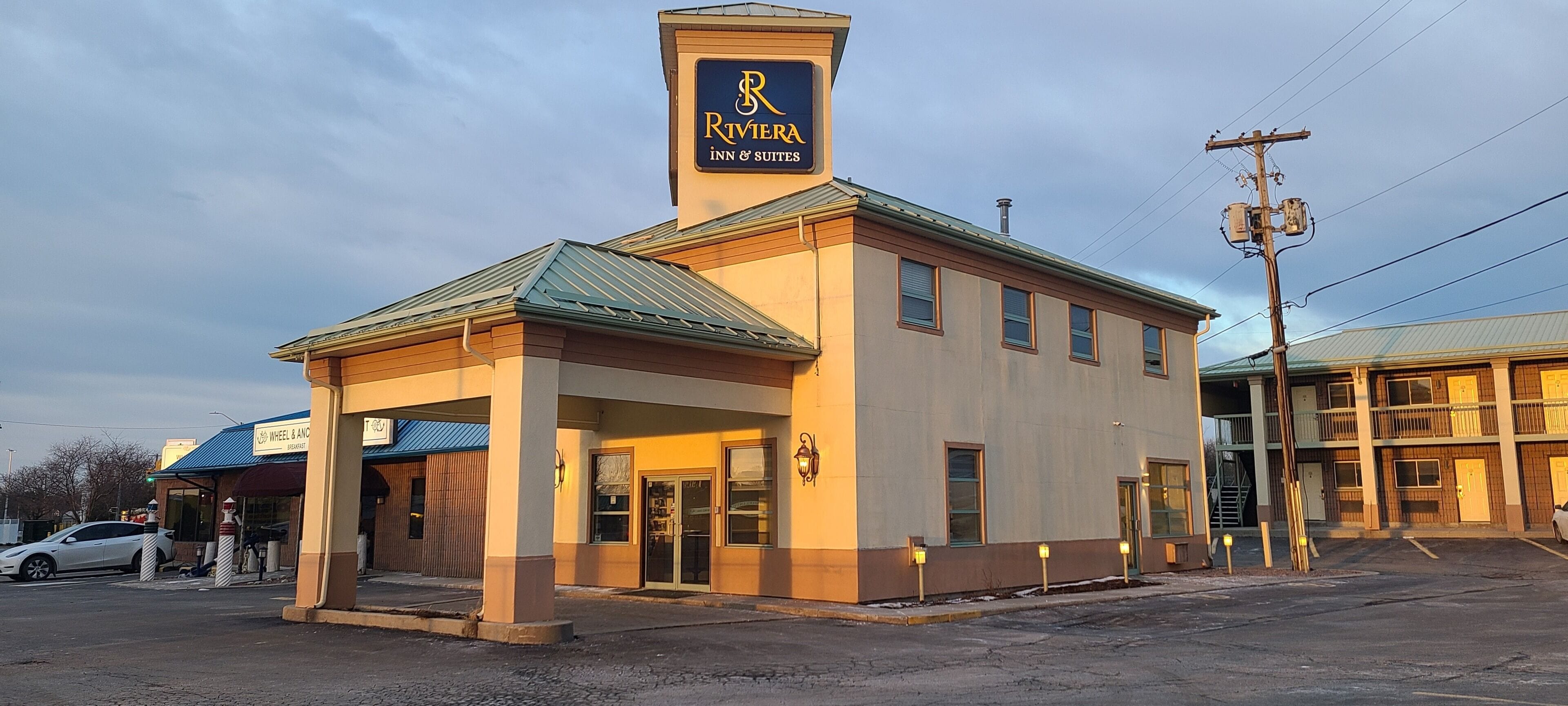 Un edificio con un cartel que dice 'Riviera Inn & Suites', que muestra un logotipo destacado y una estructura de dos pisos con techo plano.