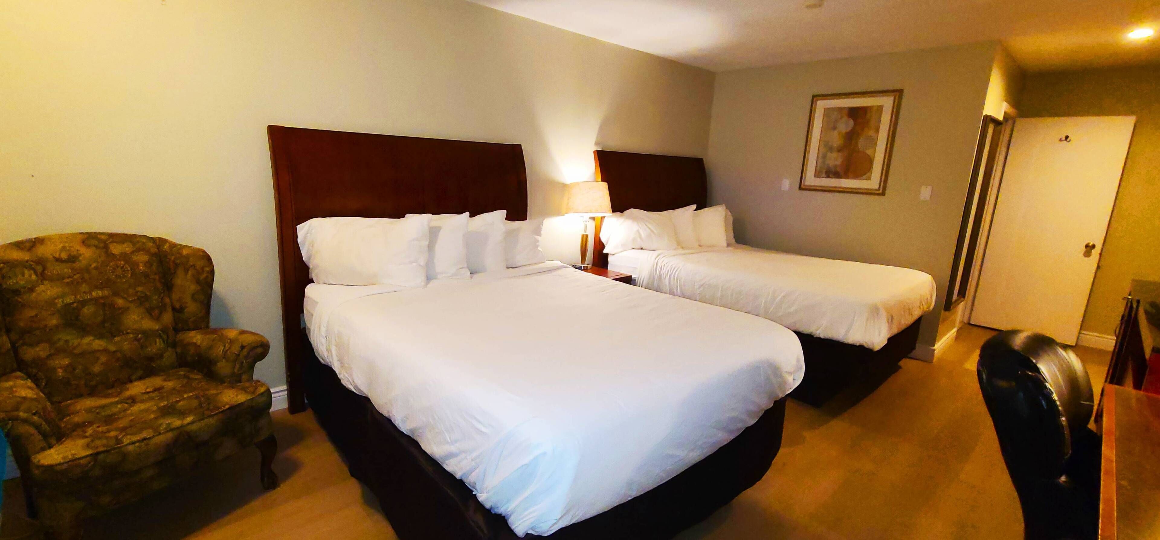 Une chambre d’hôtel avec deux lits, une chaise, une lampe et un tableau au mur.