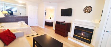 A living room with a fireplace, a TV, and a bed in the background.