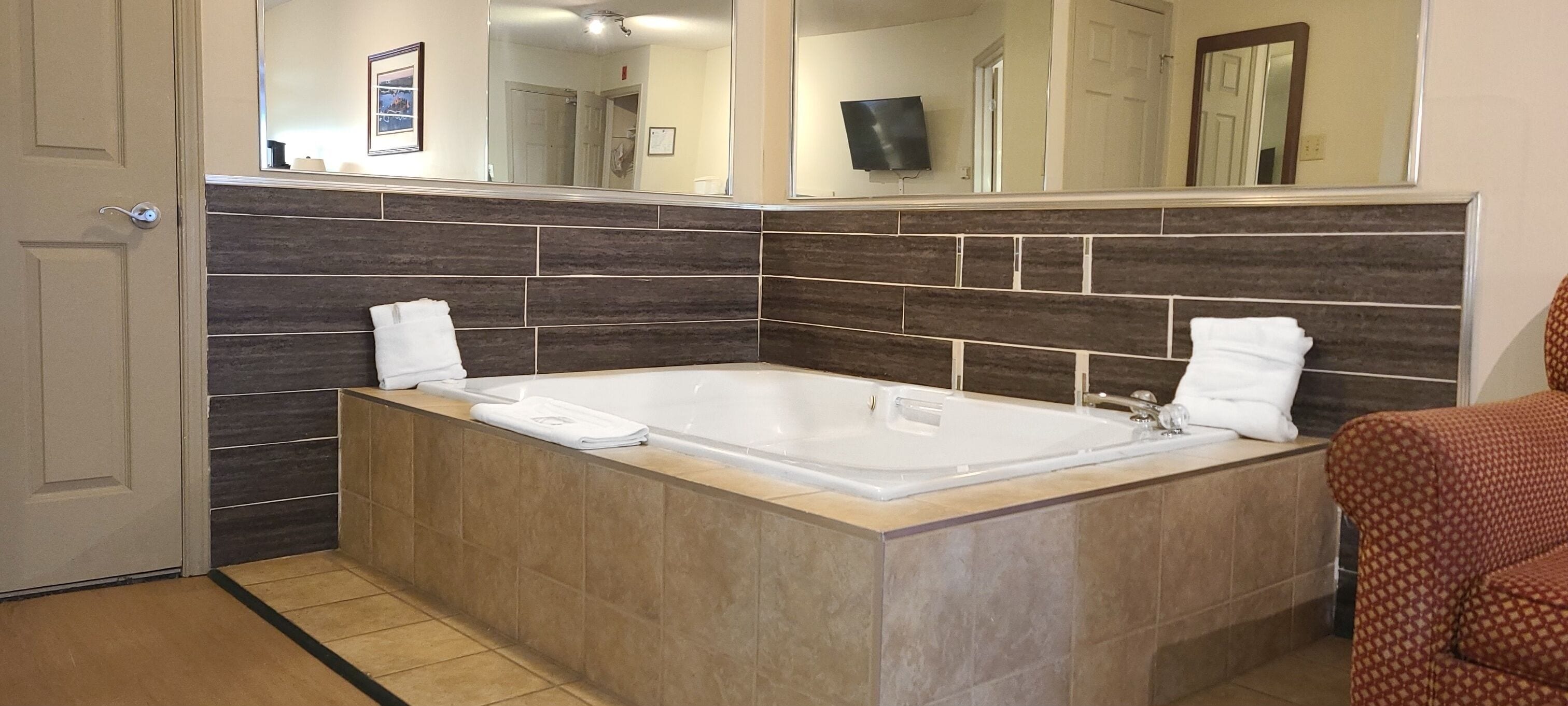 A bathroom with a large bathtub, dark tiled walls, and a mirror above the tub.