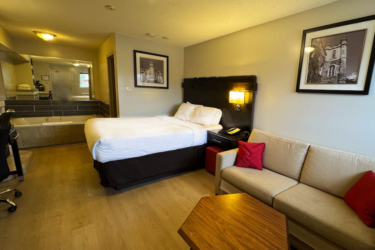 Ein Hotelzimmer mit einem Bett, einem Sofa, einem Couchtisch, einem Schreibtisch mit Lampe und gerahmten Bildern an den Wänden.
