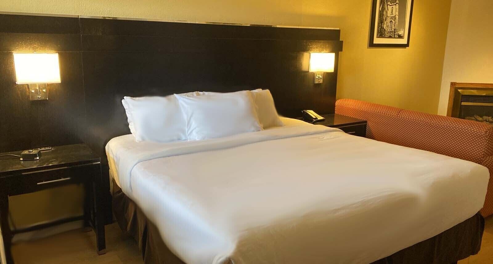 Una habitación de hotel con una cama grande, dos mesitas de noche, un teléfono y un cuadro enmarcado en la pared.