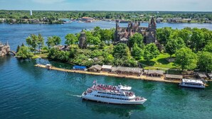 A large white boat with passengers, a historic building with pointed towers, and a river with a dock. - Riviera Inn and Suites 1000 Islands (Gananoque)