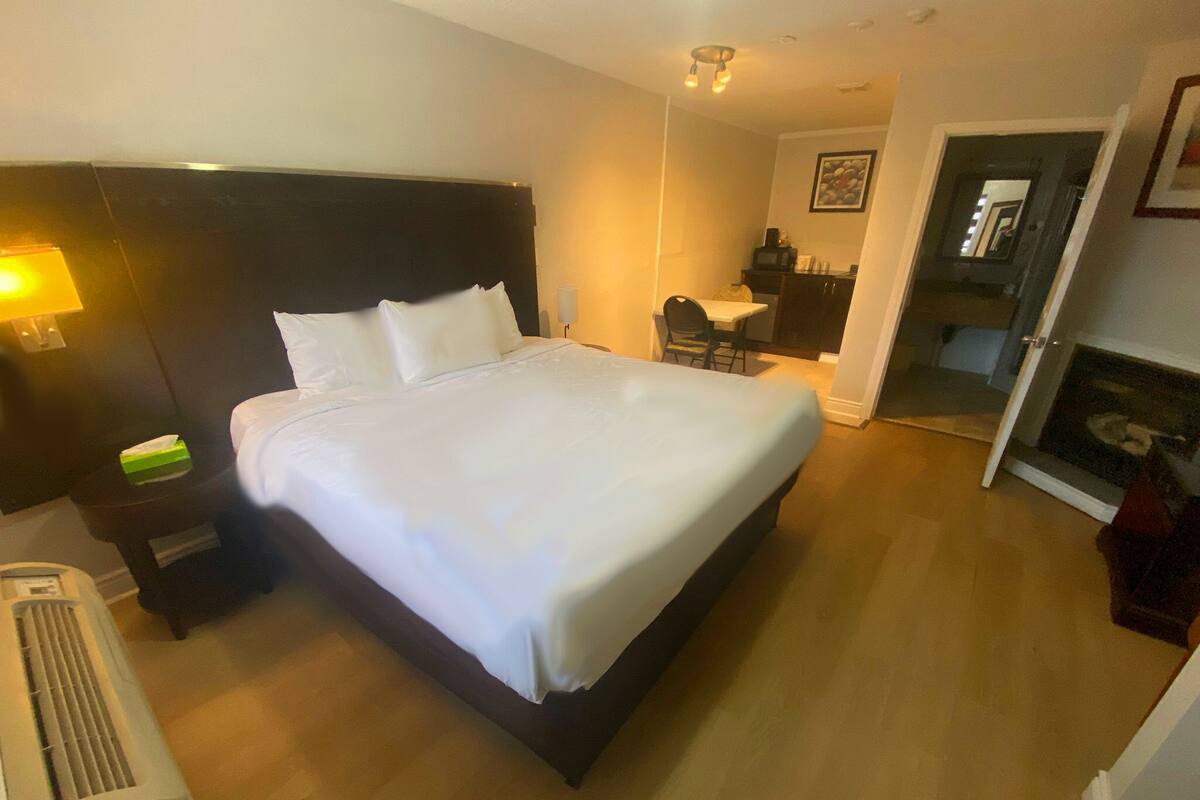 Ein Hotelzimmer mit einem großen Bett, einem Nachttisch mit Lampe, einem Sessel und einem kleinen Tisch mit Fernseher.