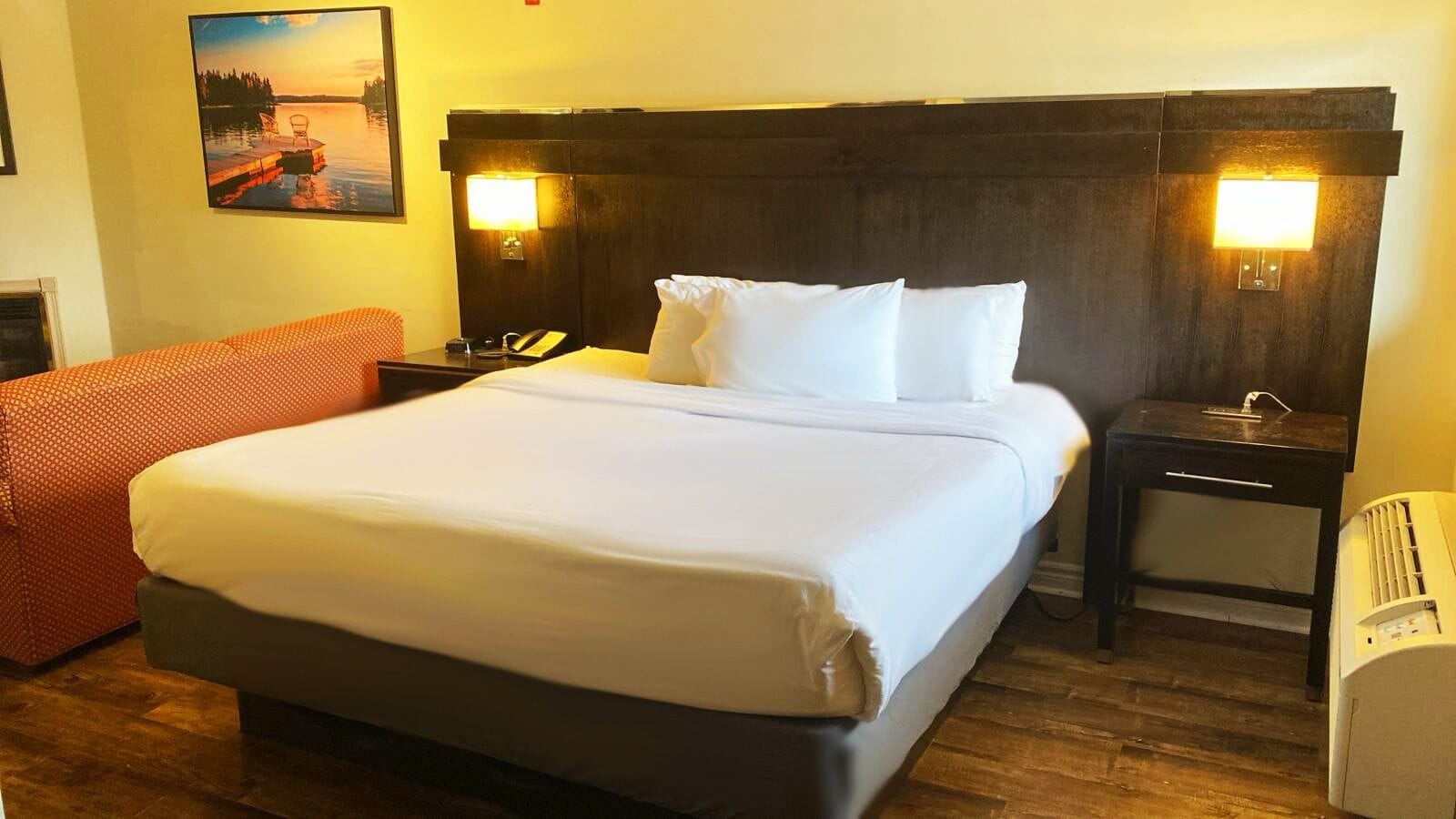 Une chambre d’hôtel avec un grand lit, deux lampes de chevet, une petite table, une chaise et un tableau au mur.
