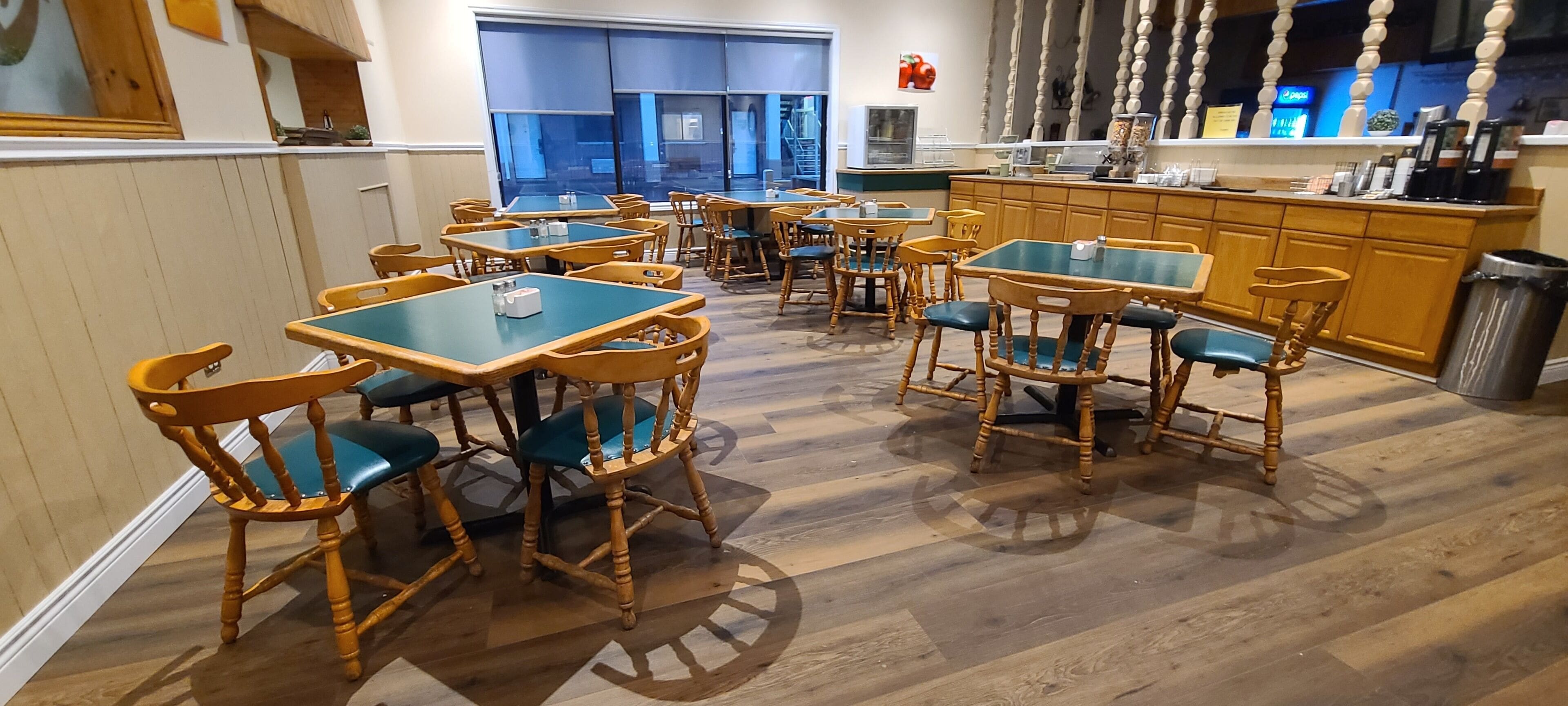 Un espace repas avec des tables et des chaises en bois, un comptoir de cuisine et une grande fenêtre.