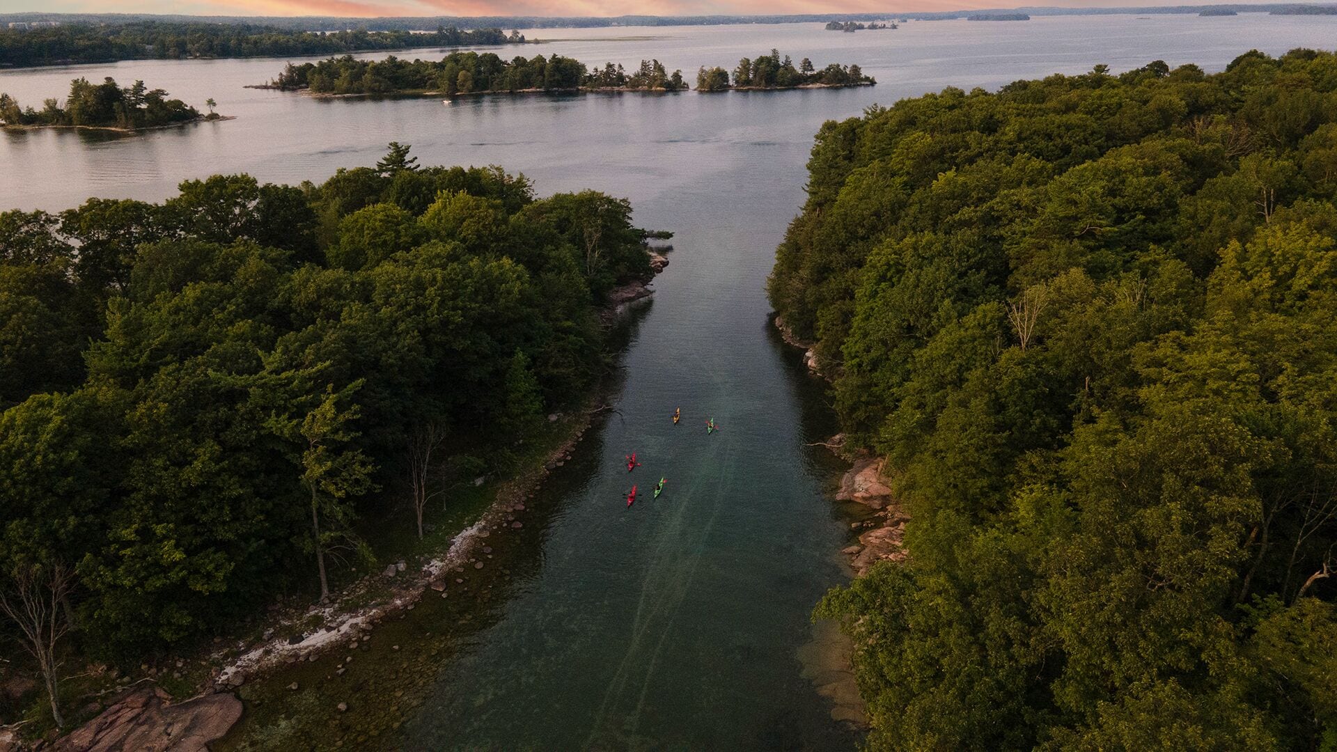 Vue aérienne d’une rivière bordée d’une forêt dense, où l’on aperçoit des personnes pratiquant le kayak.