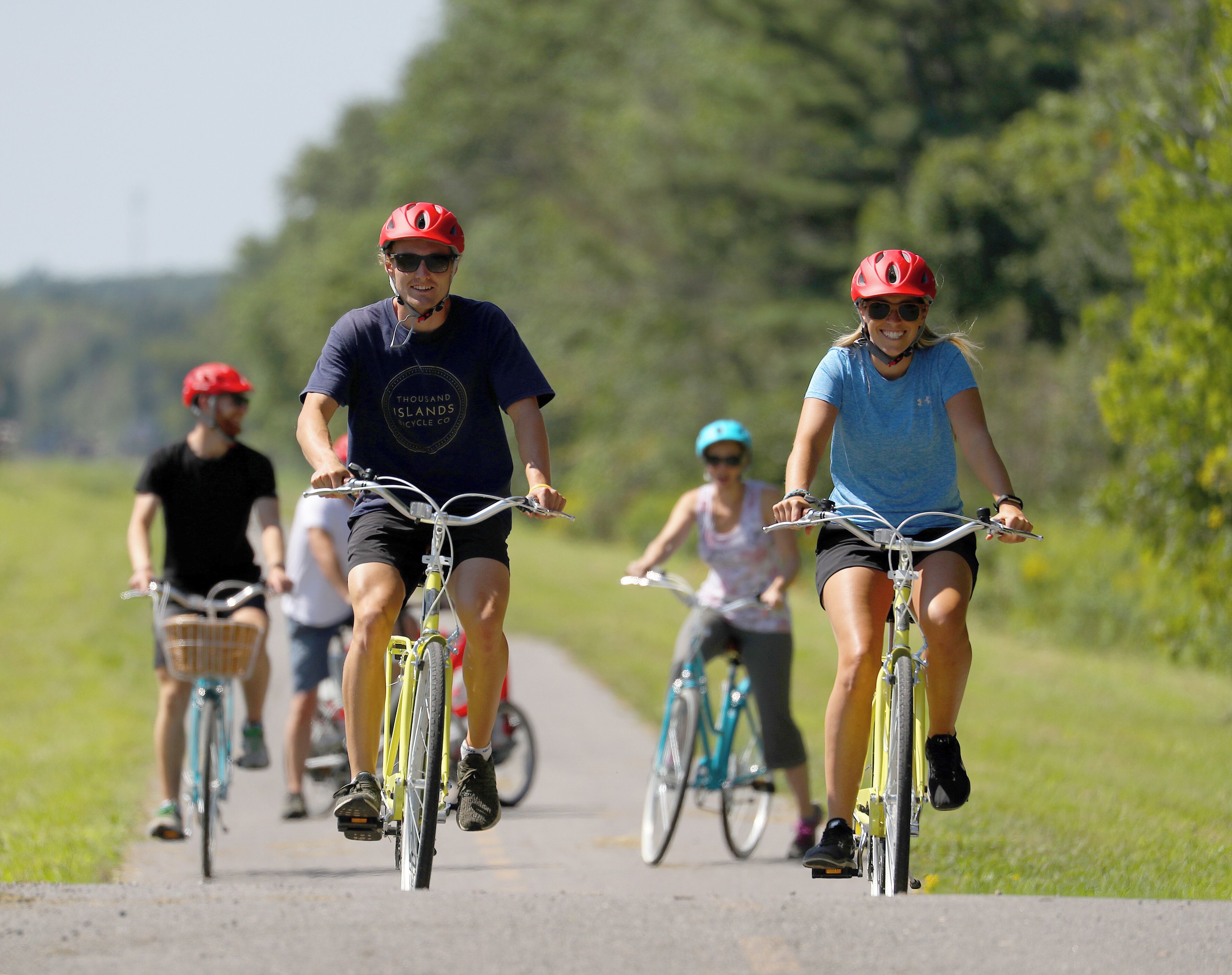A group of people riding bicycles on a paved path surrounded by greenery.