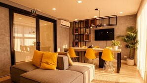 A modern living room with a sofa, yellow chairs, a dining area, and a TV mounted on the wall.