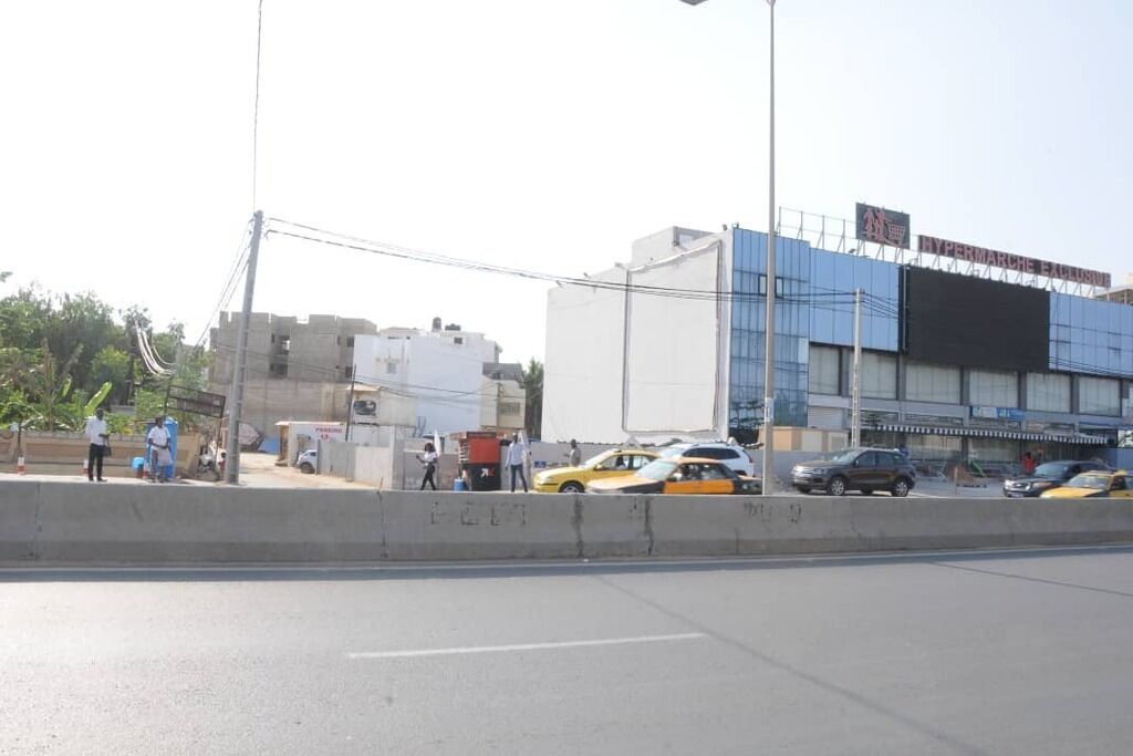 A street scene with a large building labeled "Hypermercado" and several cars parked along the road.