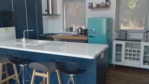 A modern kitchen with a central island, bar stools, a teal refrigerator, and a white cabinet with glass doors.