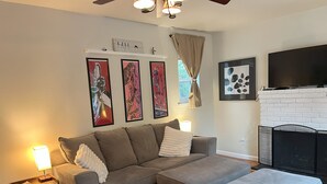 A living room with a grey sectional sofa, a small side table, a fireplace, and wall art. - Seaside Family House - Sleeps 6 on Monterey Peninsula (Seaside)