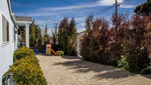 A residential driveway with a play area, including a slide and a swing set, surrounded by mature trees and a house. - Seaside Family House - Sleeps 6 on Monterey Peninsula (Seaside)
