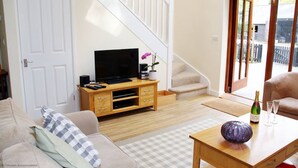 A living room with a TV, wooden entertainment unit, sofa, and a table with a bottle and glasses. - Middledown -  a cottage that sleeps 7 guests  in 3 bedrooms (Newton Valence)
