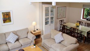 A living room with two sofas, a table with chairs, a lamp, and a cabinet with glass doors. - Middledown -  a cottage that sleeps 7 guests  in 3 bedrooms (Newton Valence)