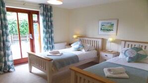 A bedroom with two beds, a window with curtains, a bedside lamp, and a painting on the wall. - Middledown -  a cottage that sleeps 7 guests  in 3 bedrooms (Newton Valence)