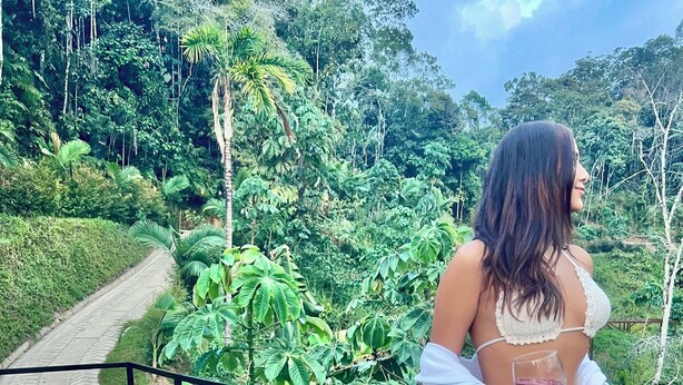 A woman standing on a balcony with a lush garden view, holding a glass of wine. - Gaia glamping  (San Rafael)
