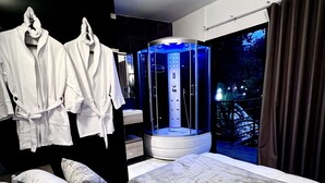 A modern hotel room with a bed, two robes, a massage chair, and a view of a garden. - Gaia glamping  (San Rafael)