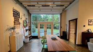 A dining area with a long wooden table, green chairs, and a view through large glass doors to an outdoor area. - THE HIDDEN COTTAGE Private, Relaxing, Great Location, Has Everything You Need (Saugerties)