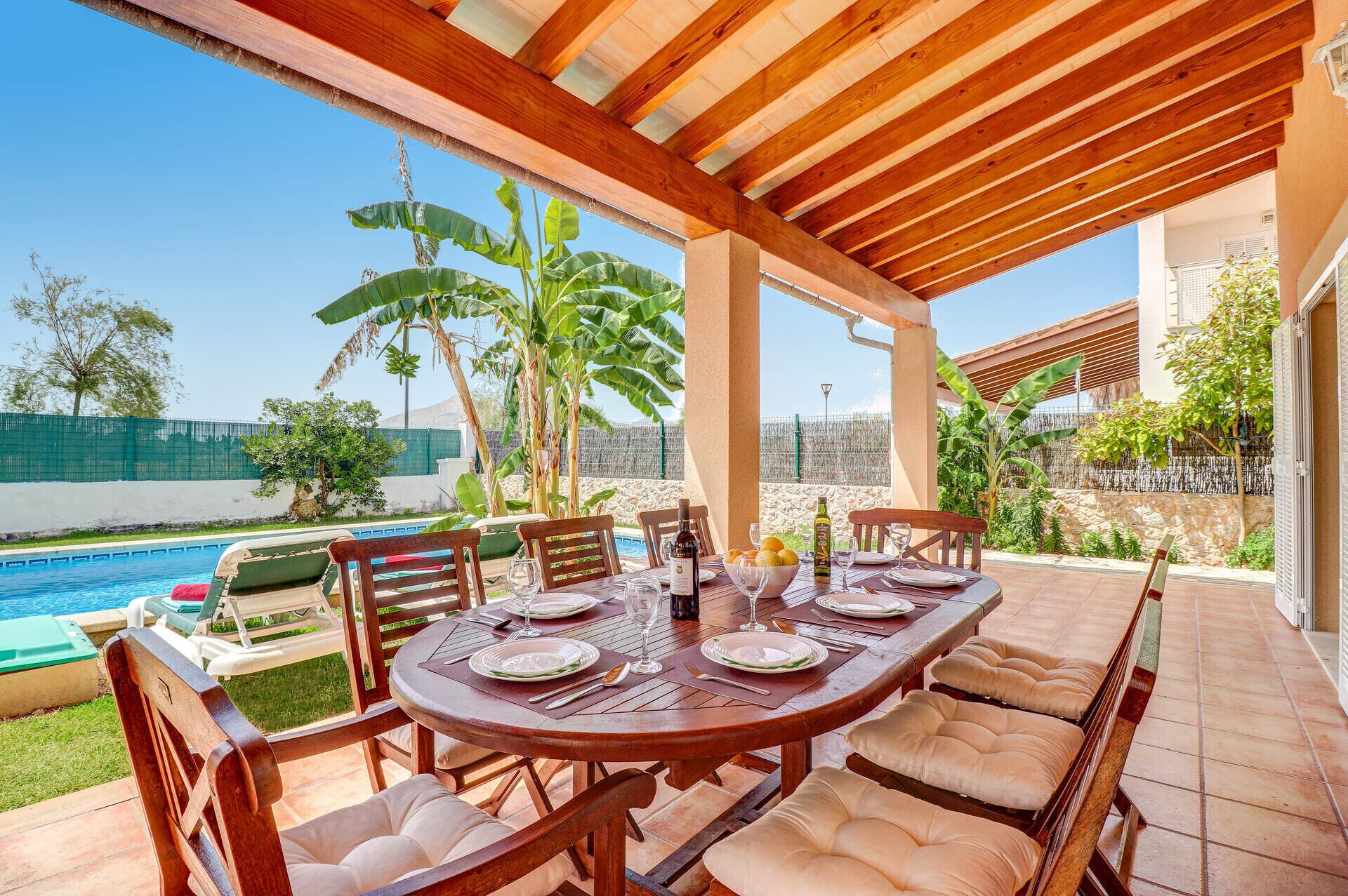A covered outdoor dining area with a pool in the background.