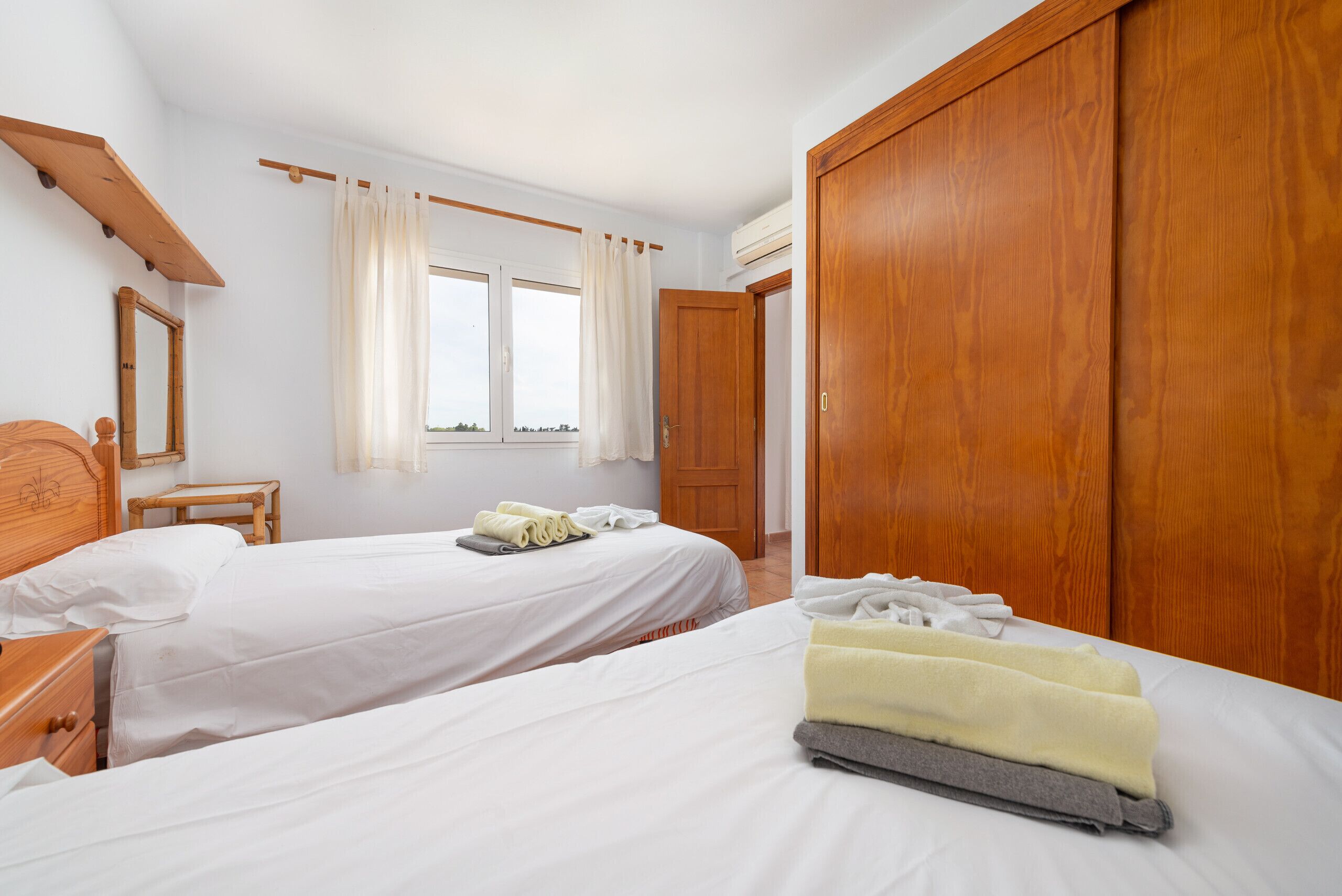 A hotel room with two beds, wooden wardrobe, a window with curtains, and a wooden headboard.