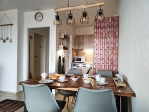 Un coin repas avec une table en bois, quatre chaises et une cuisine en arrière-plan.