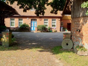Edifício de tijolos com porta azul, calçada e pequeno jardim com vasos de plantas.