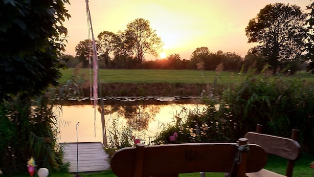A wooden bench by a pond with a wooden deck and a metal lamp post. - Ferienhaus am See (Kirchlinteln)