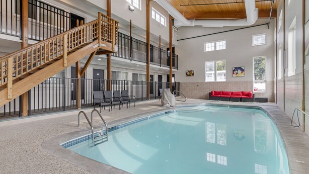 An indoor swimming pool with a wooden staircase, seating area, and a view of the outside. - Downtown Dover Inn (Dover)
