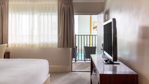 A hotel room with a bed, a TV on a wooden stand, a balcony with a pool view, and a door leading to a common area. - Downtown Dover Inn (Dover)