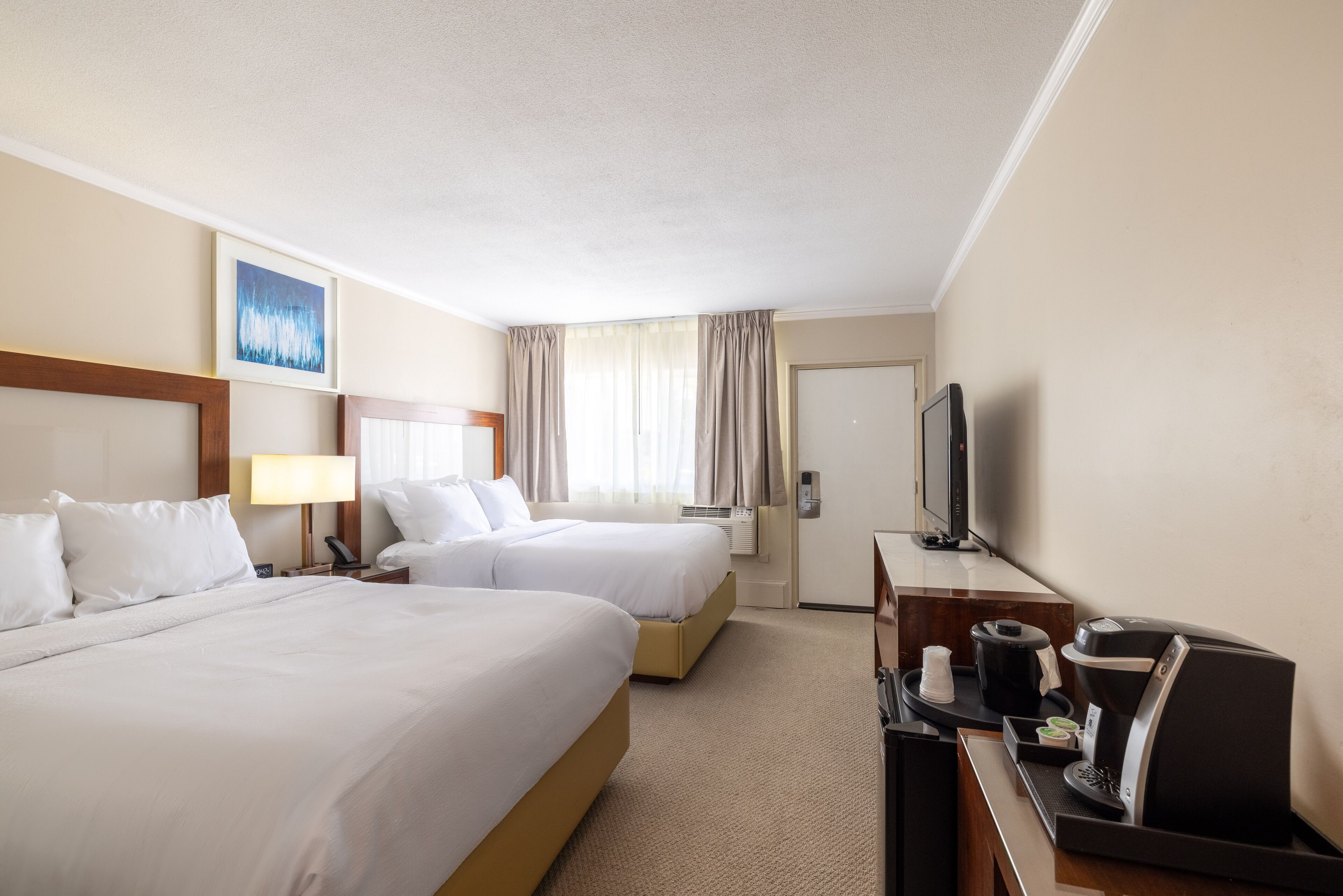A hotel room with two beds, a desk with a coffee maker, a television, and a window with curtains.