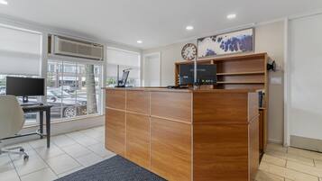 A reception desk with a computer, a clock, and a window view of a parking lot.