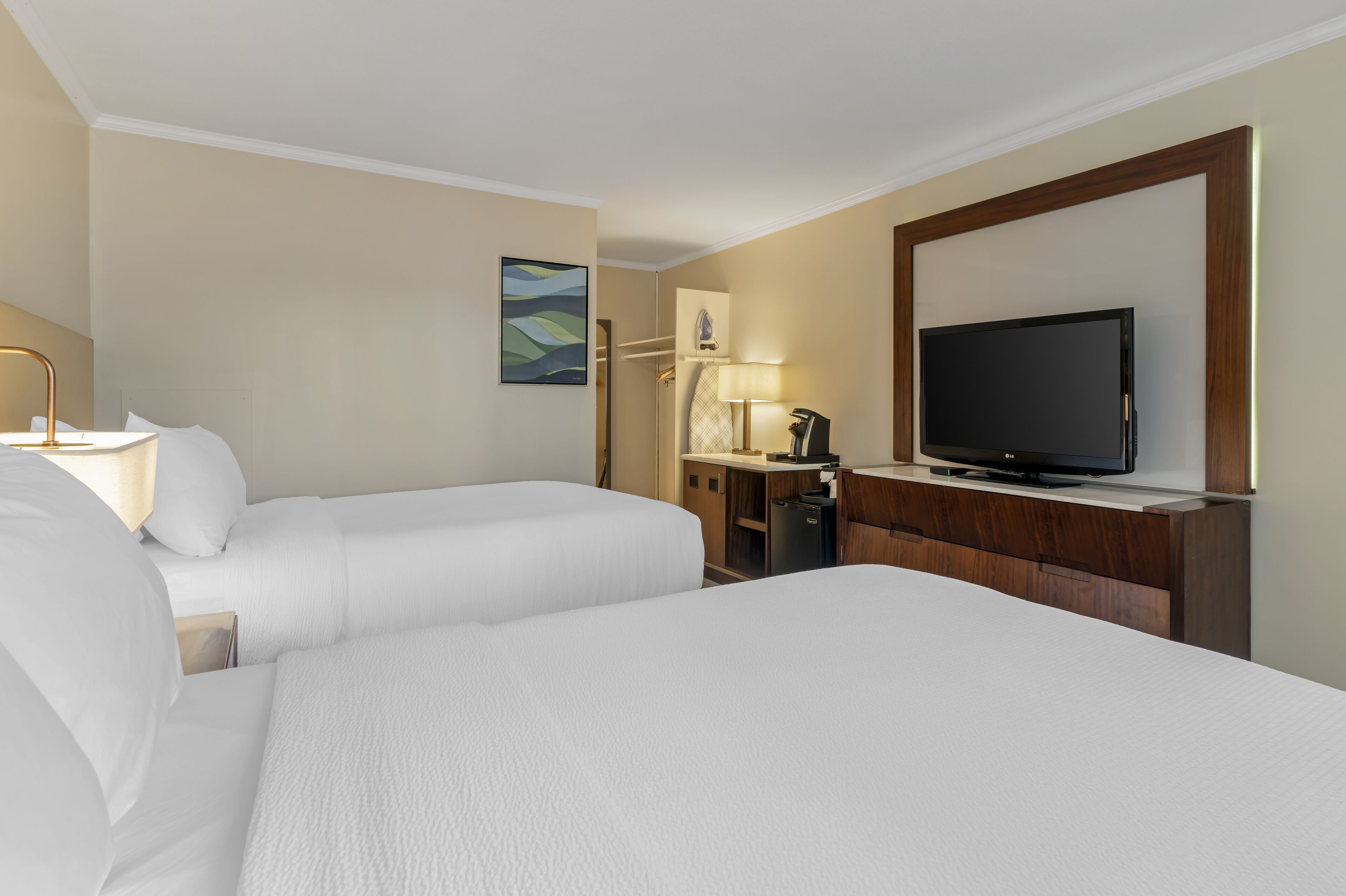 A hotel room with two beds, a TV, a desk with a lamp, and a painting on the wall.