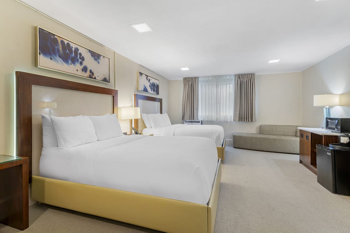 A hotel room with two beds, a desk, a chair, and a TV.