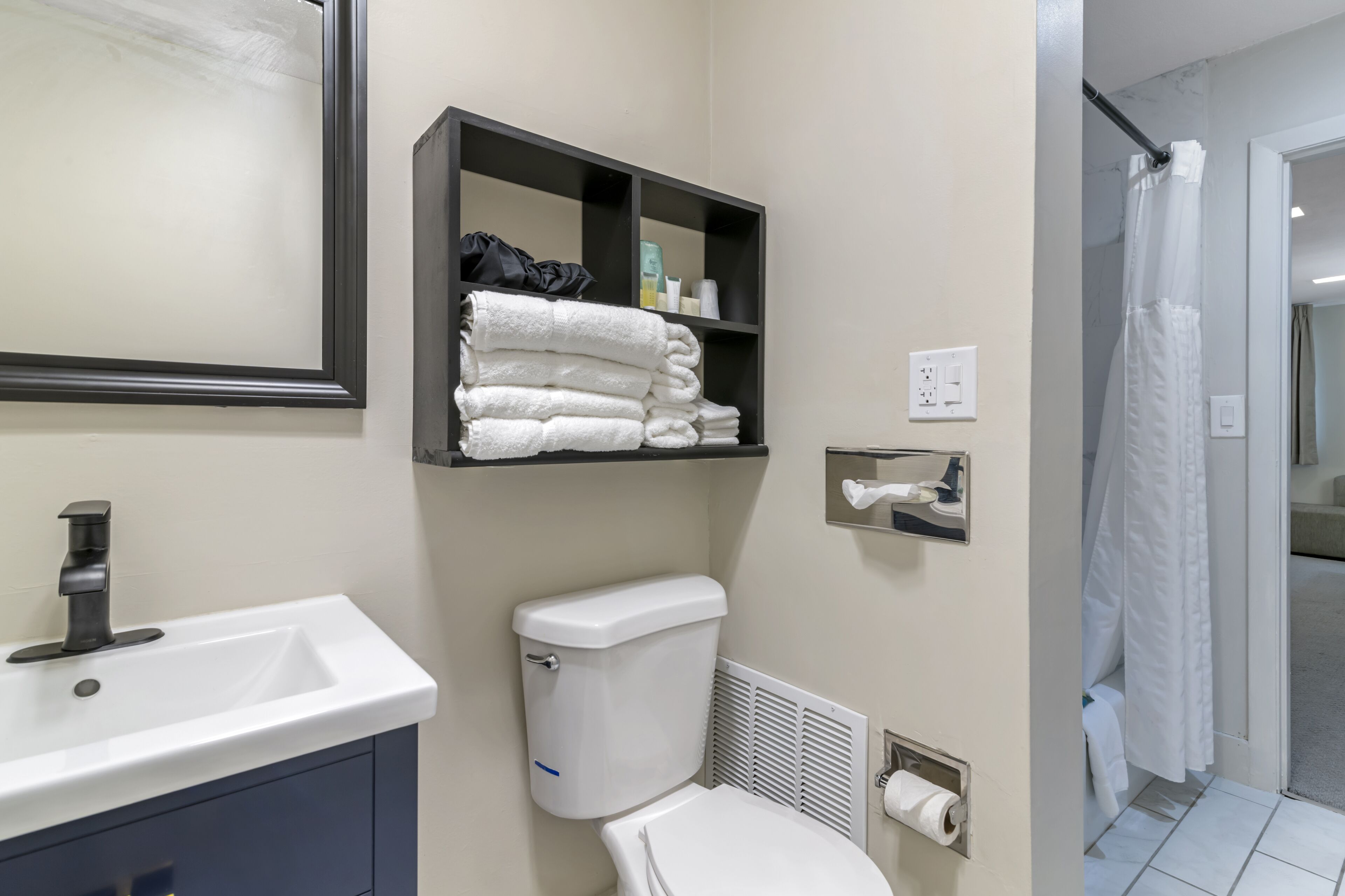 A modern bathroom with a white sink, a toilet, a towel rack with folded towels, and a shower area.