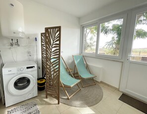 A laundry area with a washing machine, a drying rack, and a window with a view of greenery. - Apartamento Acolhedor bem Localizado com Pátio Exterior no Centro de Lagos (Lagos)