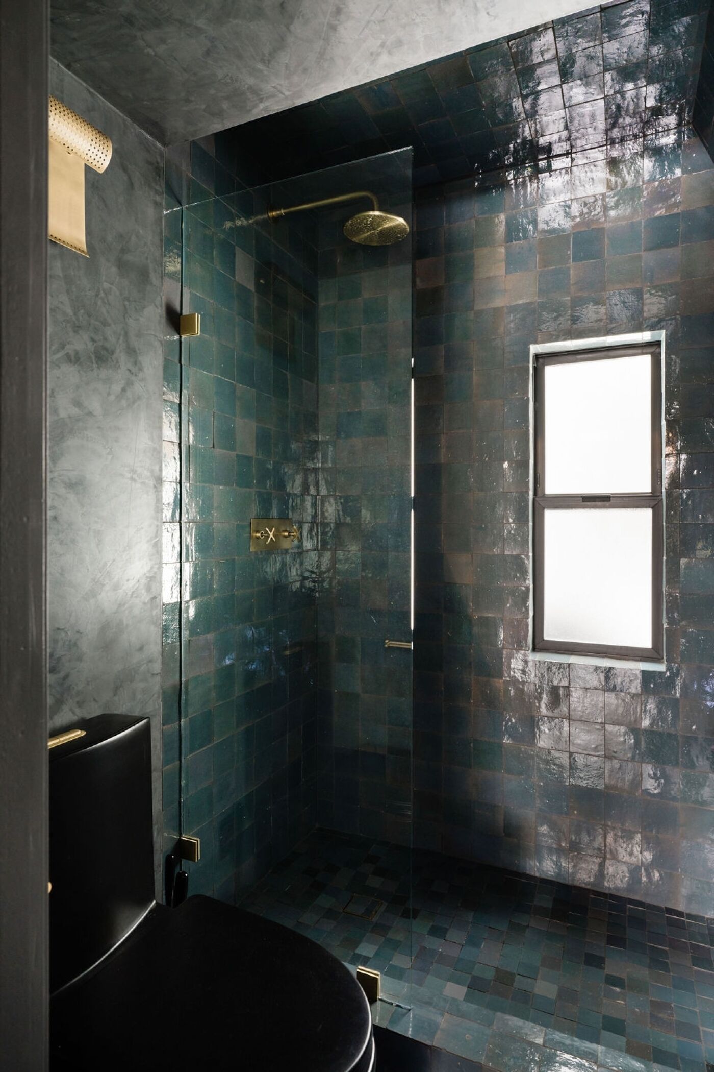 A modern bathroom with a glass-enclosed shower, a black toilet, and a window providing natural light.