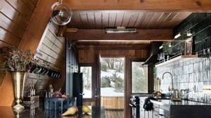 A modern kitchen with wooden accents, a bar area, and a view of the outdoors. - Romantic A-Frame Cabin w/ Hot Tub, Fire Pit, Boulders, Fireplace, Hiking, Skiing (Running Springs)