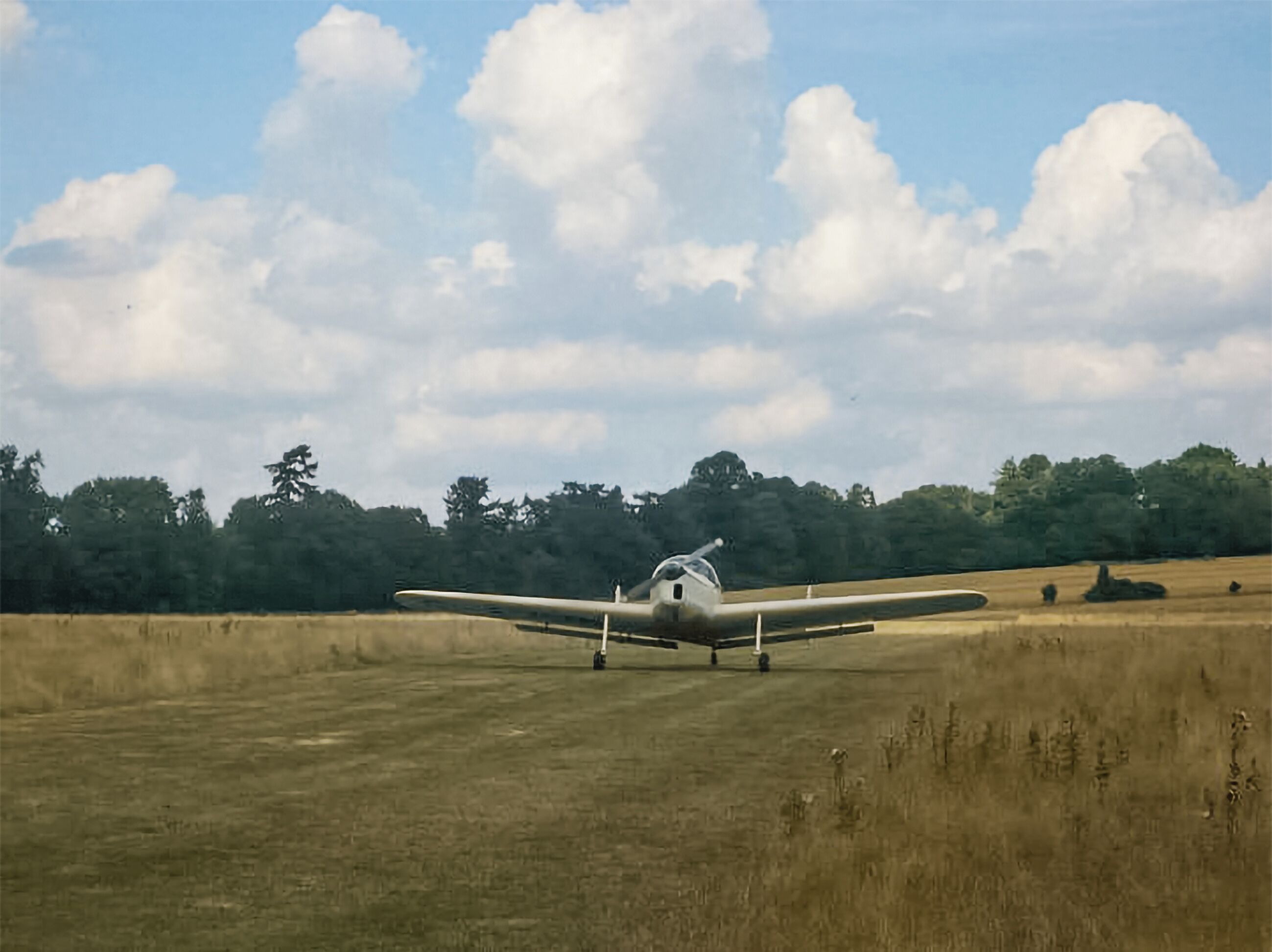 Un petit avion se trouve sur un champ d’herbe, avec des arbres en arrière-plan.