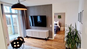 A modern living room with a flat-screen TV, a sofa, a dining area with a table and chairs, and a potted plant. - The World Appartment (Magdeburg)
