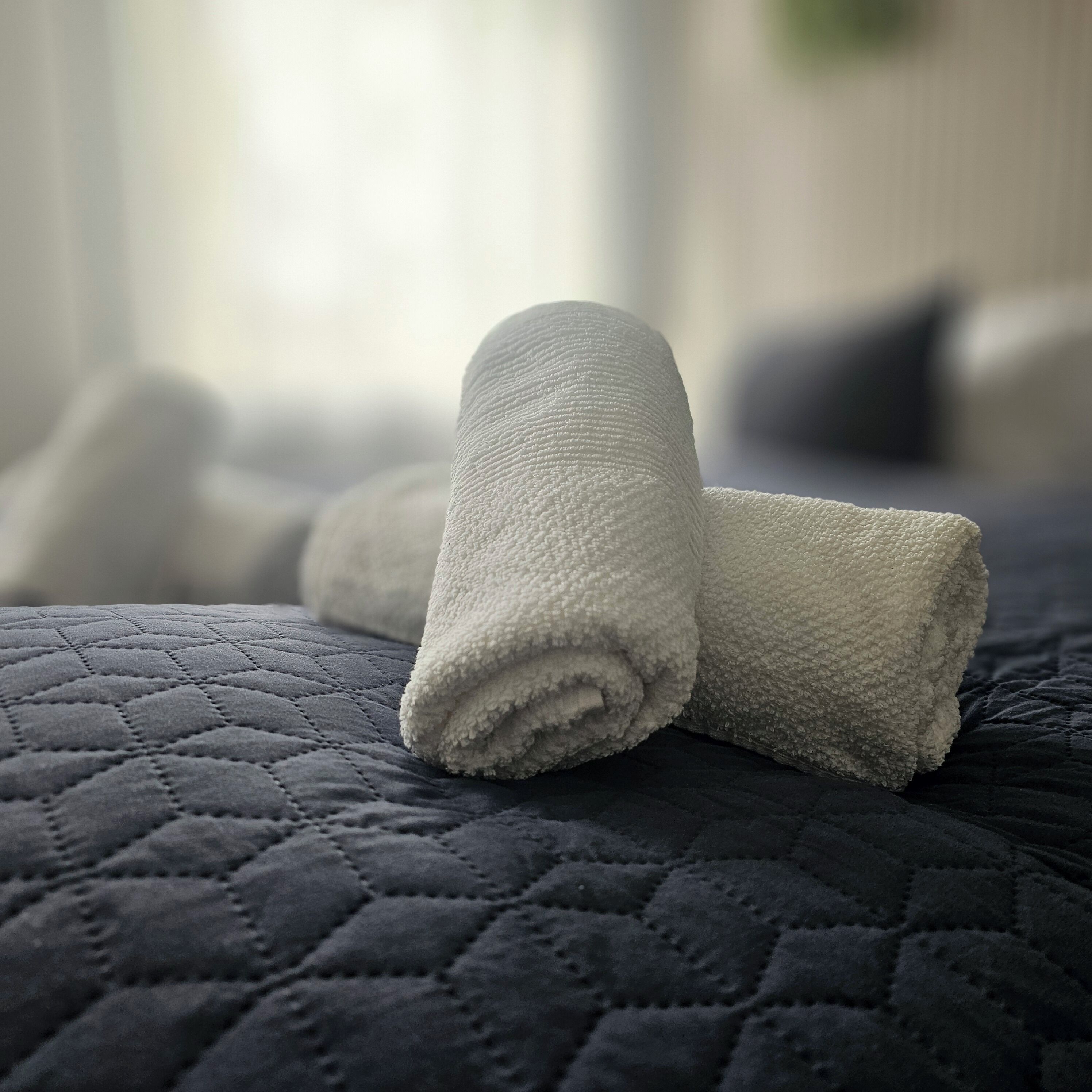 A neatly folded white towel on a dark quilted bedspread in a hotel room.