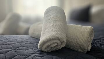 Ein ordentlich gefaltetes weißes Handtuch auf einer dunkel gesteppten Hotelbettdecke.