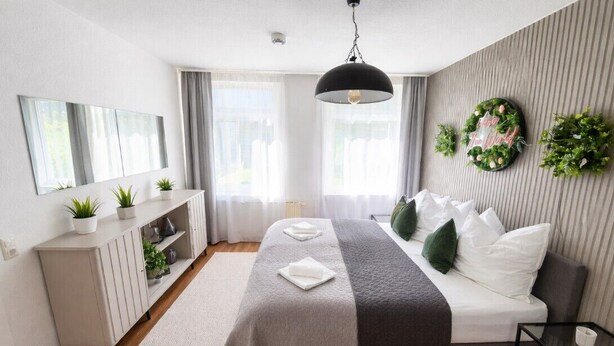 A modern bedroom with a bed, bedside tables, a mirror, and a wall-mounted light fixture. - The World Appartment (Magdeburg)