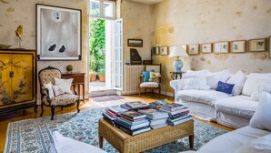 Una sala de estar acogedora con sofá, sillón y una mesa de centro con libros. Se ve un ventanal con vistas a la vegetación.