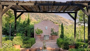 Ein Garten mit Brunnen, einer Pergola und einer Statue.