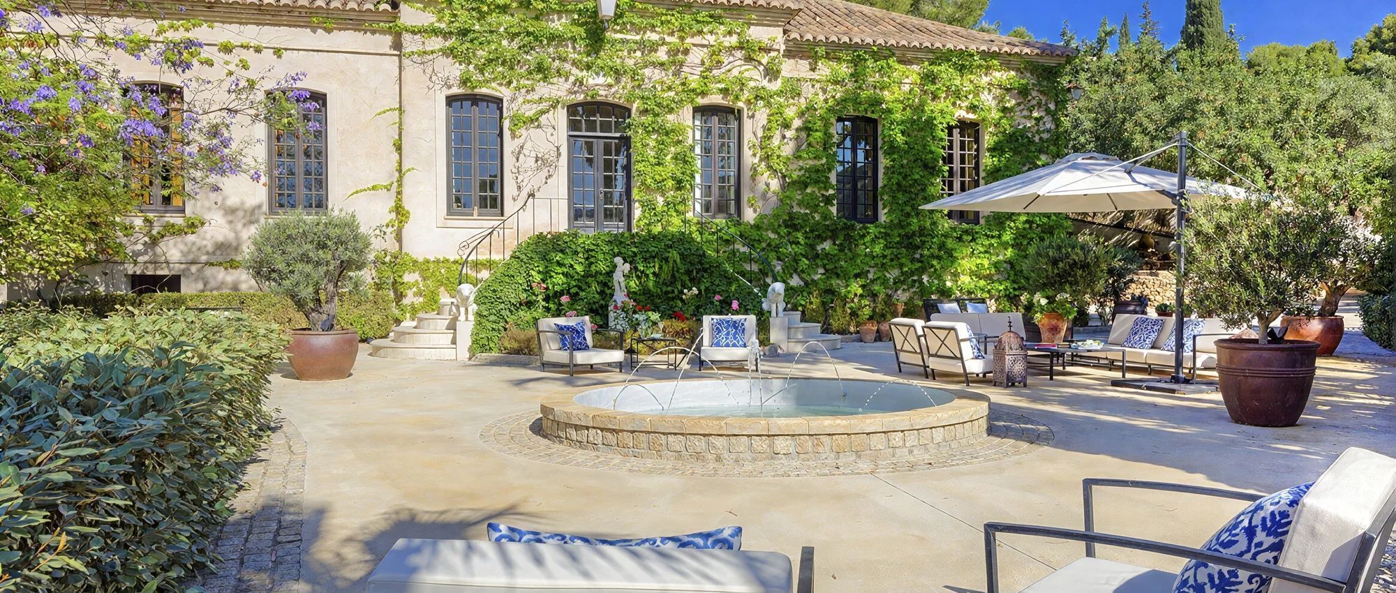 A courtyard with a fountain, outdoor seating, and a building with arched windows.
