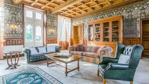 A spacious living room with a high wooden ceiling, two sofas, a coffee table, and a large cabinet with glass doors. - Chateau Serbise Estate (Belluire)