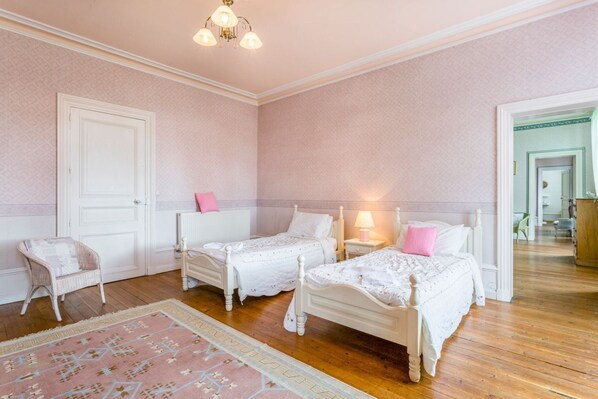 A bedroom with two white beds, a pink rug, and a white chair.