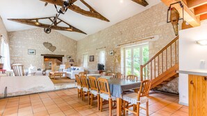A spacious dining area with a long table and chairs, a stone wall, and a staircase leading to an upper level. - Chateau Serbise Estate (Belluire)