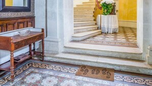 A grand staircase with a chandelier, a wooden bench, and a patterned floor. - Chateau Serbise Estate (Belluire)